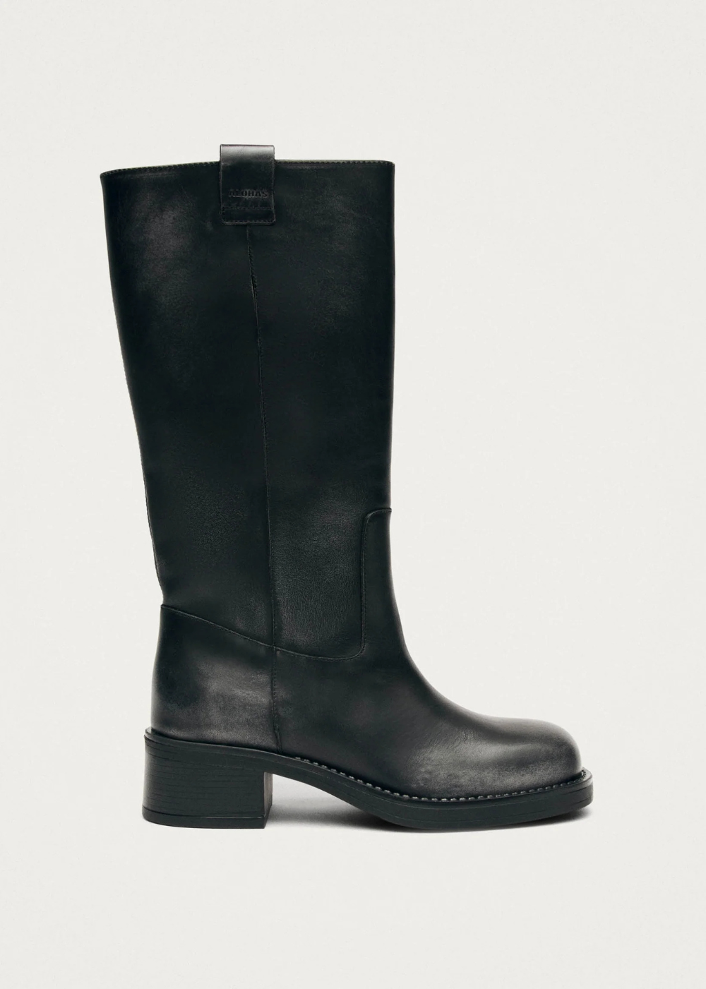 A black leather knee-high boot with a block heel and a small pull tab at the top, shown from a side profile against a light gray background.
