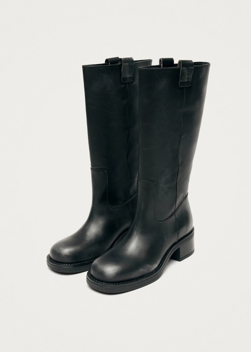 A pair of black leather knee-high boots with low block heels and side pull tabs, photographed on a light gray studio background.