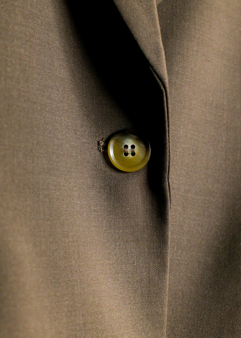 Close-up of a taupe-brown suit jacket with a single round, translucent olive-green button on a dark lapel.