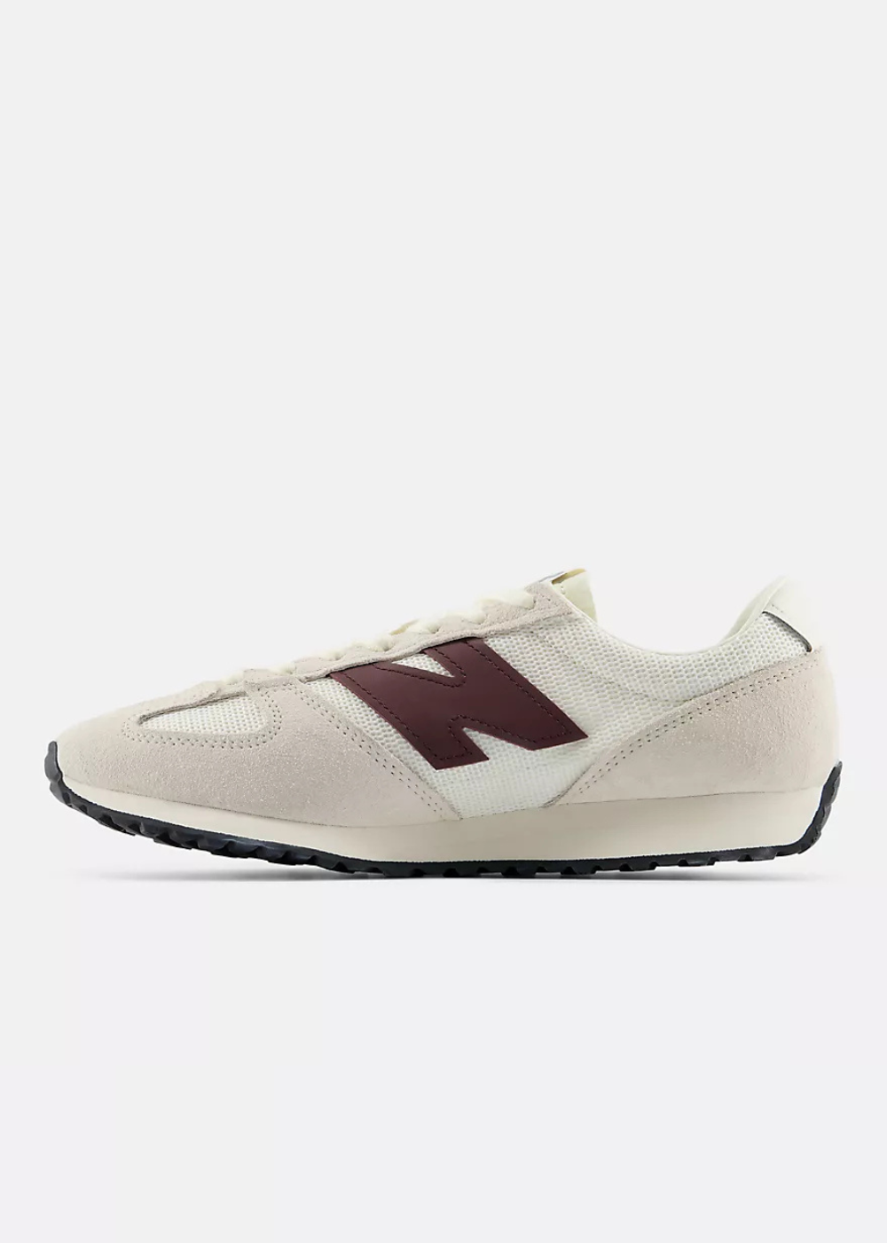 A New Balance sneaker in off-white suede and mesh with a dark burgundy 'N' logo on the side, shown in profile against a light gray background.