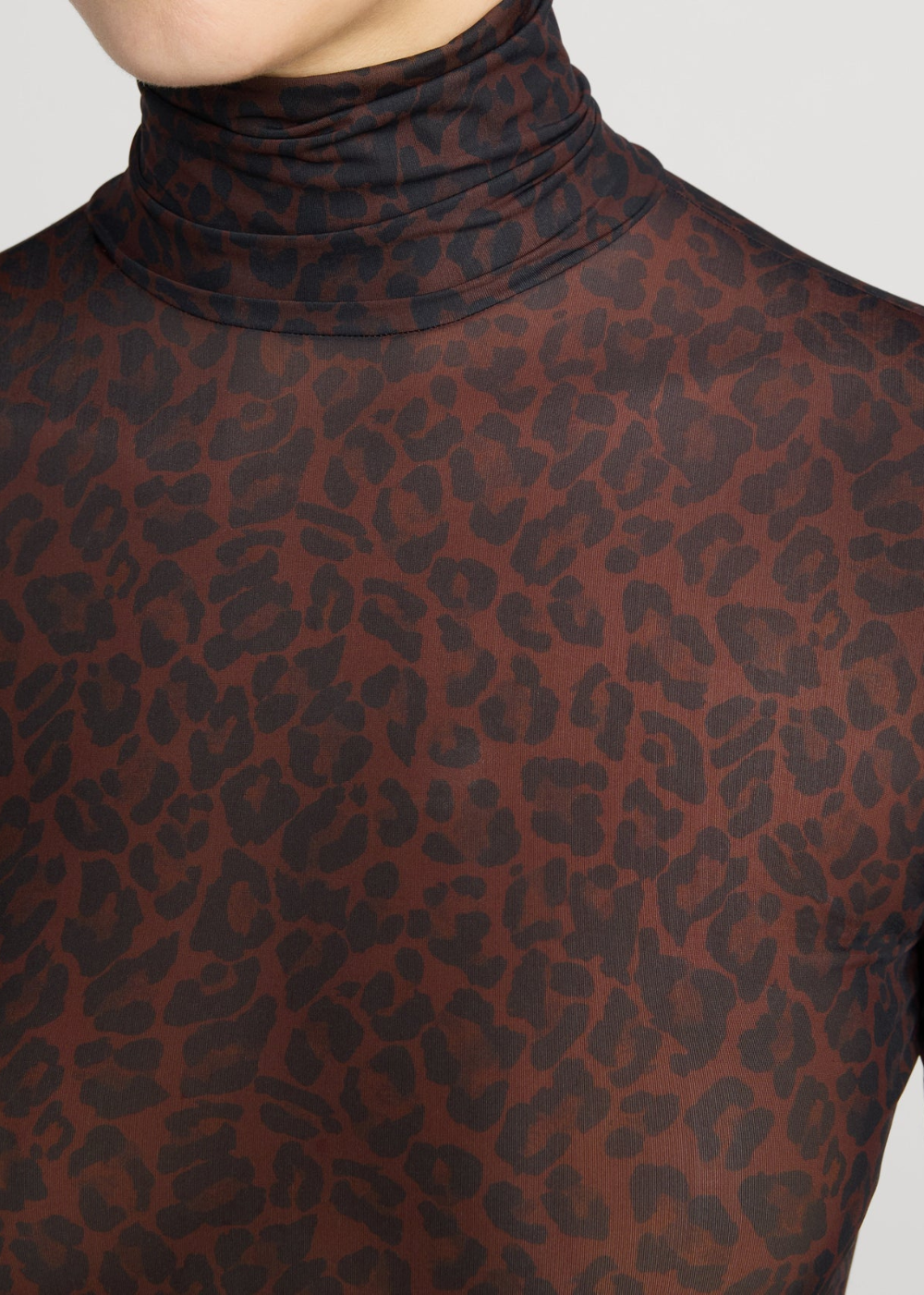 Close-up of a sheer brown turtleneck top with a dark leopard print pattern, worn by a model.