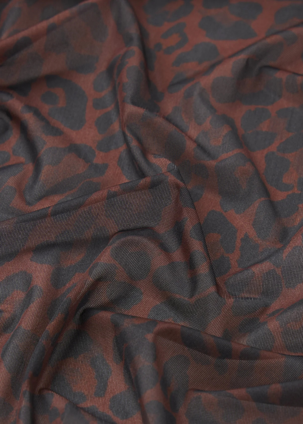 A close-up of draped fabric with a dark charcoal gray leopard print pattern over a warm rust brown base.