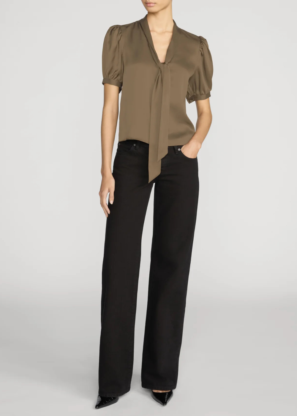 A model wearing a short-sleeved, olive-brown satin blouse with puffed sleeves and a front tie detail, paired with black wide-leg trousers and black pointed-toe heels, against a light gray studio background.