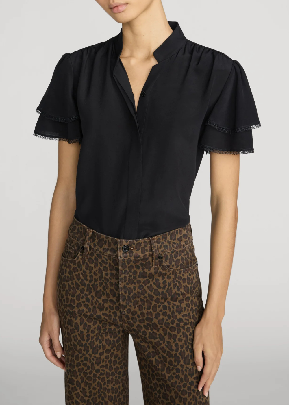 A model wearing a black short-sleeve blouse with ruffled flutter sleeves and leopard-print pants, cropped from the mouth down against a light gray studio background.